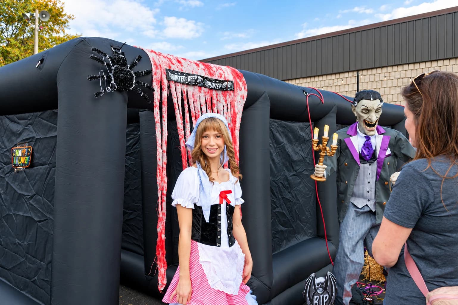 A smiling guest in a white bonnet and pink-and-white costume stands beside the haunted-house entrance.