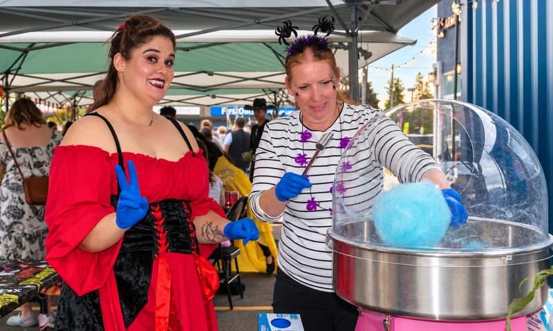 Two costumed adults make blue cotton candy under the event tent.
