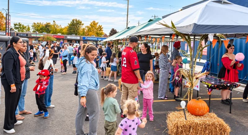 Families move between decorated activity tents, with cotton candy and pumpkins in view.
